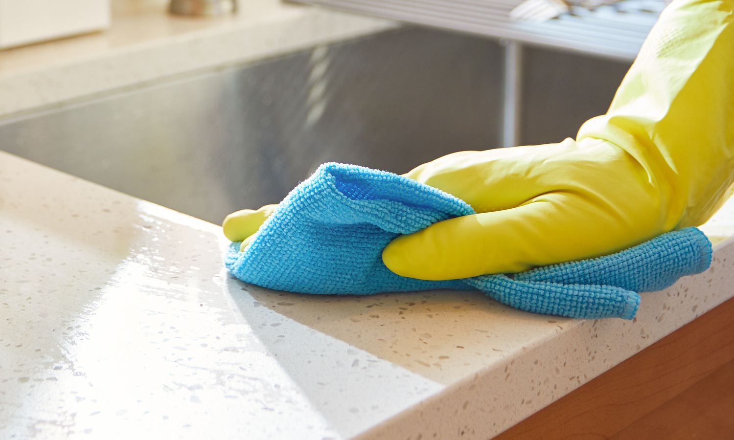 A house cleaner cleaning and sanitizing kitchen worktop and surfaces wearing rubber gloves and using a blue towel