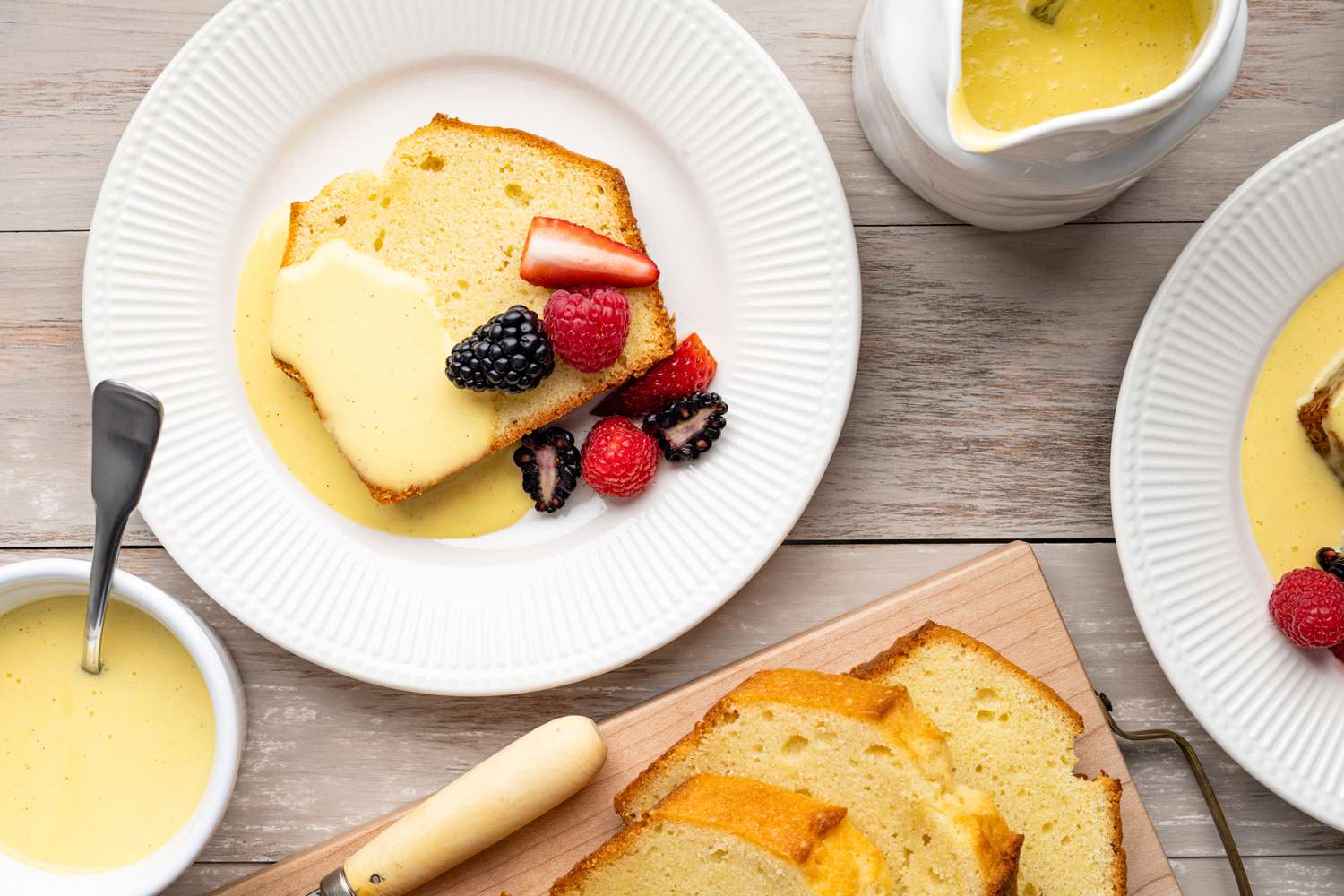 Plate of Pound Cake Covered with Creme Anglaise and Fruits, Surrounded by a Bowl of Crème Anglaise and a Platter of More Pound Cake