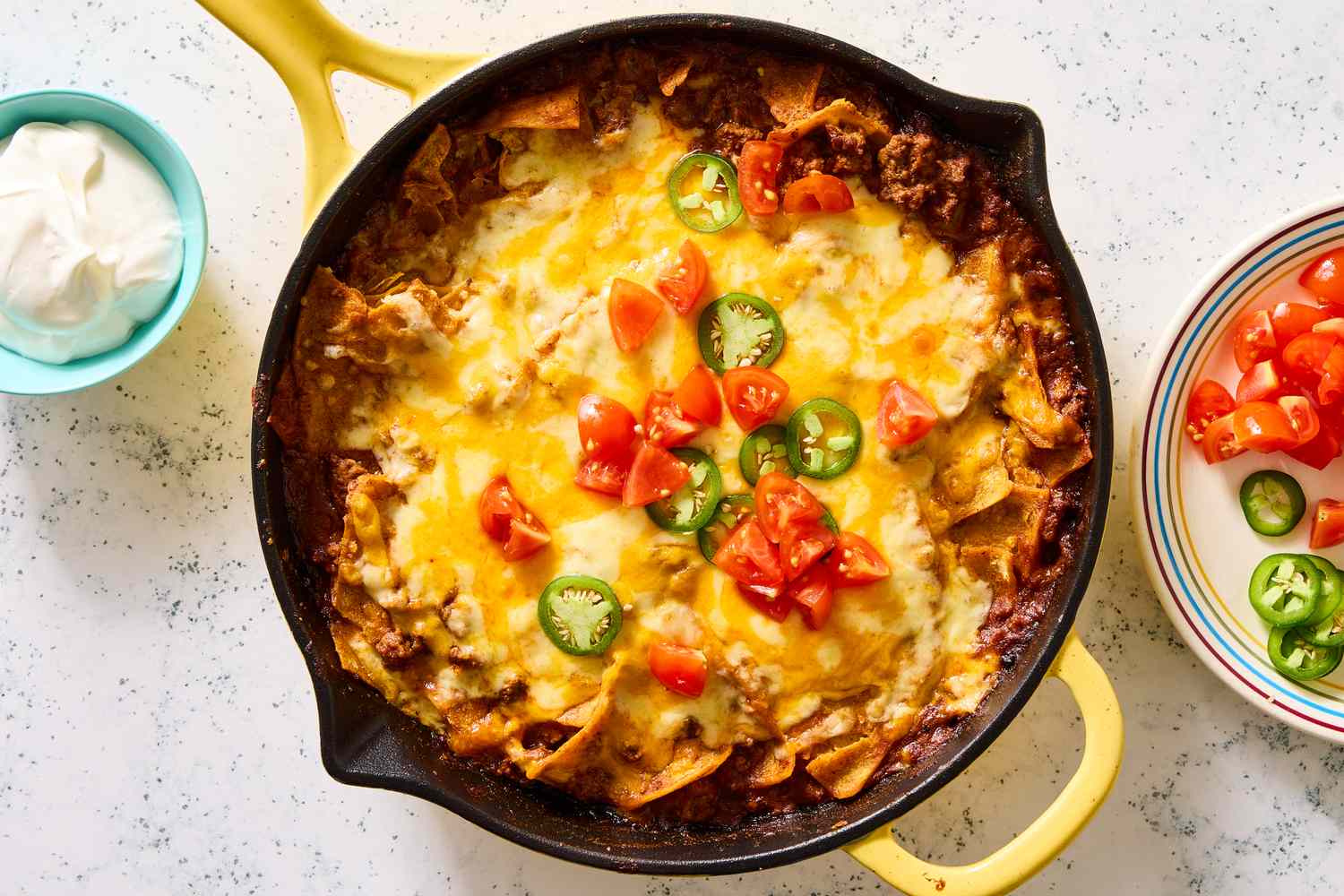 Beef enchilada skillet topped with melted cheese, chopped tomatoes, and jalapenos