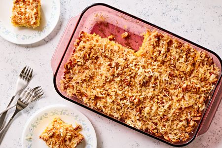 Overhead view of a glass baking dish of pineapple coconut cake with two slices removed next to two small plates with slices along with three forks