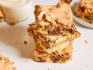 Stack of dessert bars with a meringue top and chocolate chips on a tabletop near a glass of milk
