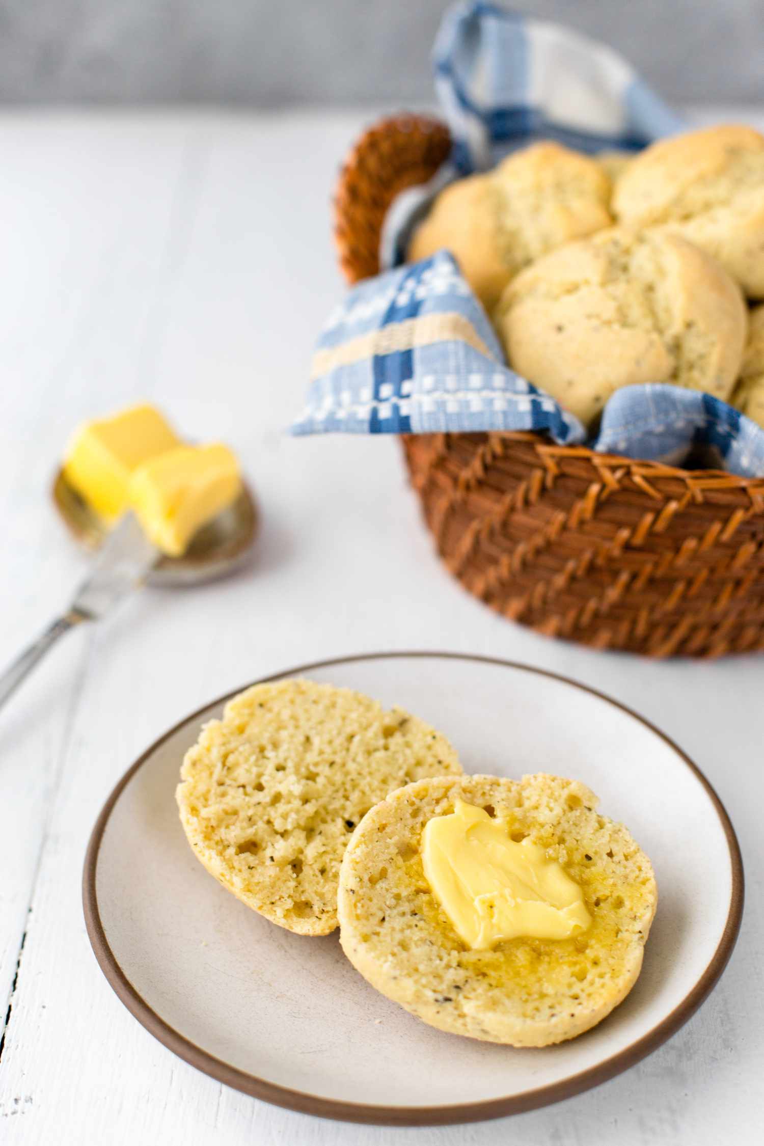 Gluten-Free Dinner Roll Cut in Half, Slathered with Butter and in the Background, More Rolls in a Basket and Butter in a Butter Dish