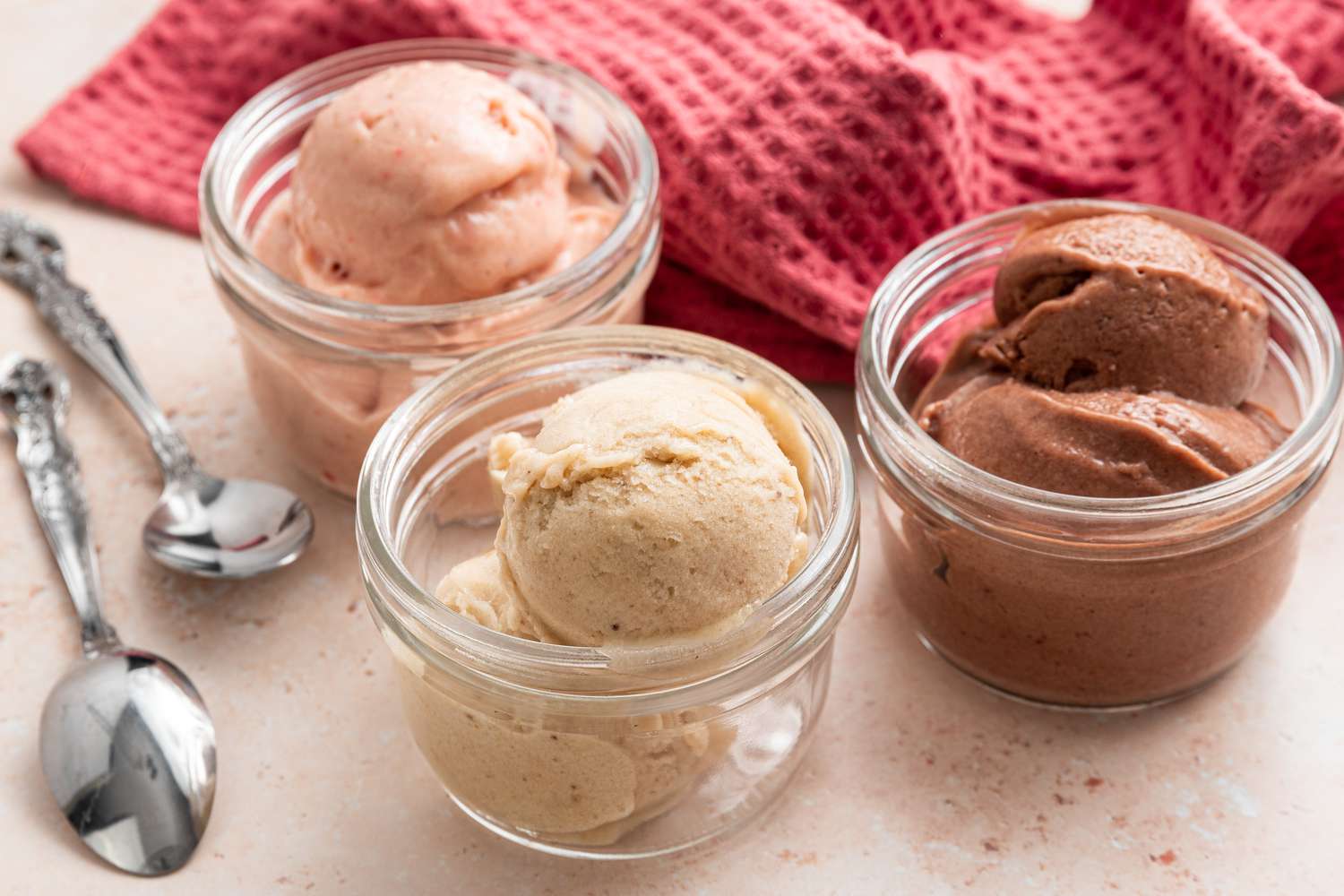 Banana Nice Cream Variations in Three Small Bowls Next to Two Spoons and a Kitchen Towel