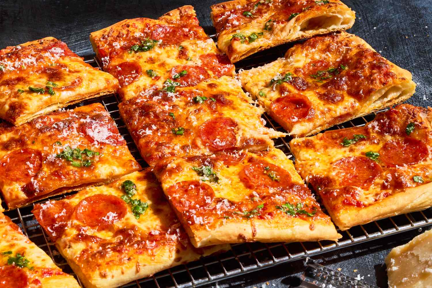 Square slices of puff pastry pizza with pepperoni and herbs on a cooling rack