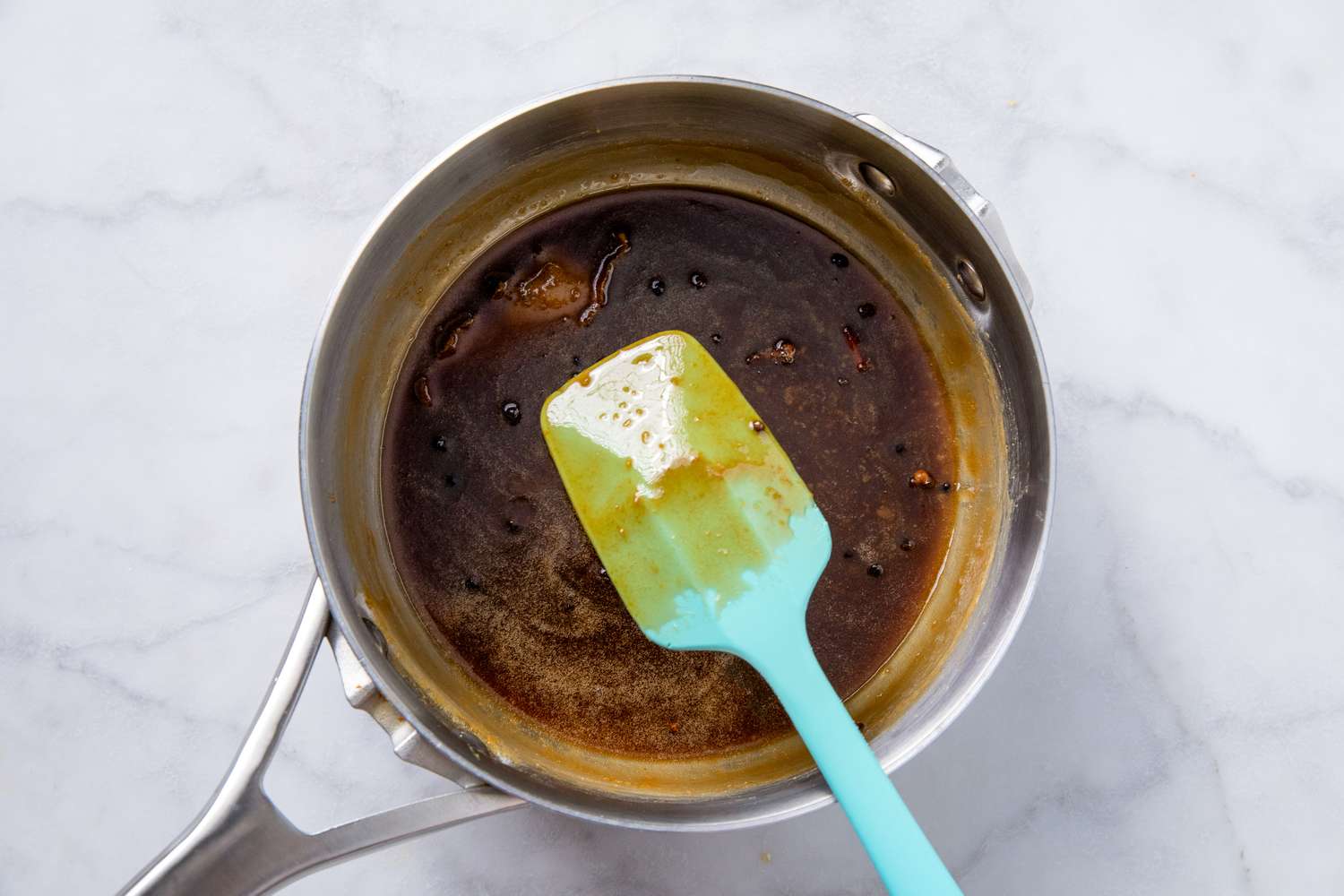 Sauce pan with brown mixture being stirred by a light blue spatula likely preparation for a recipe