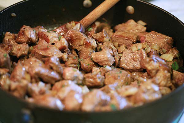 Pork cubes being cooked and stirred with garlic and onions in a skillet