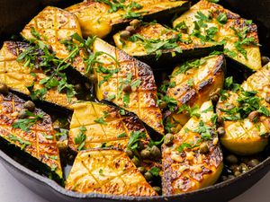 Sautéed zucchini pieces in a skillet garnished with herbs and capers