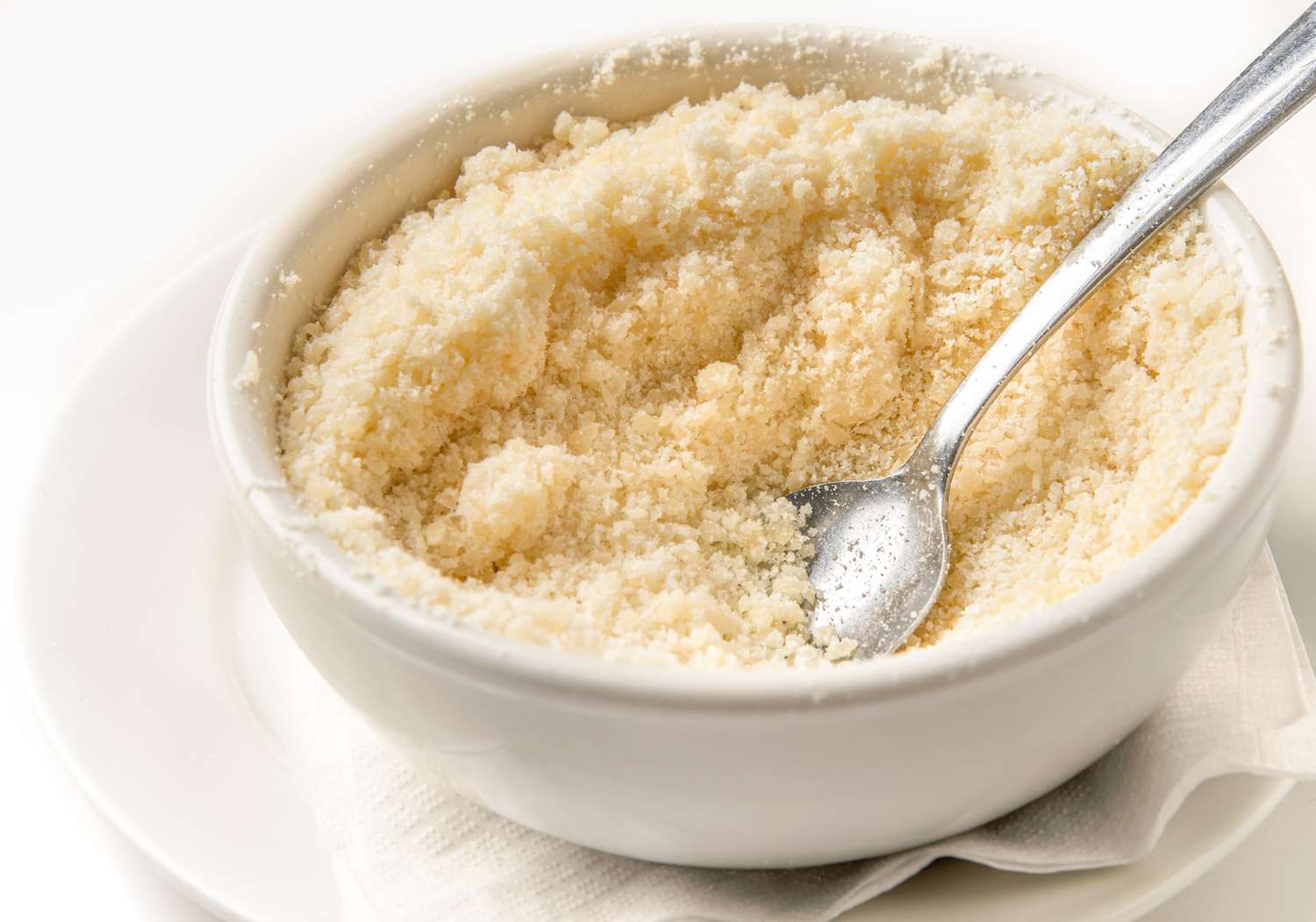 A bowl of grated cheese with a spoon inside placed on a plate