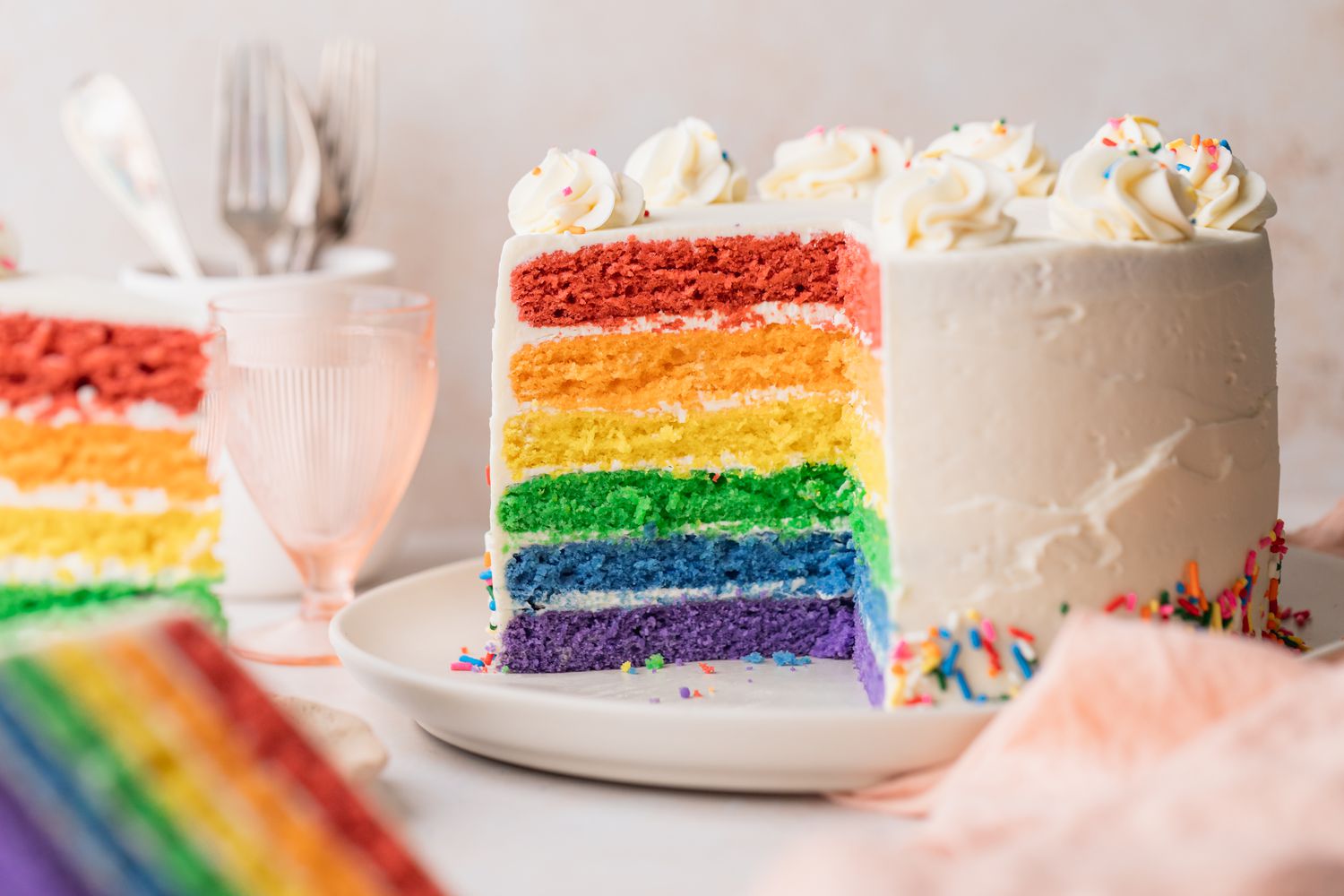Rainbow Layer Cake on a Plate with a Portion Cut Out, Surrounded by More Cake