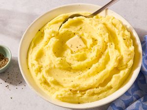 Mashed potatoes in a bowl topped with a piece of butter and black pepper a spoon placed in the dish