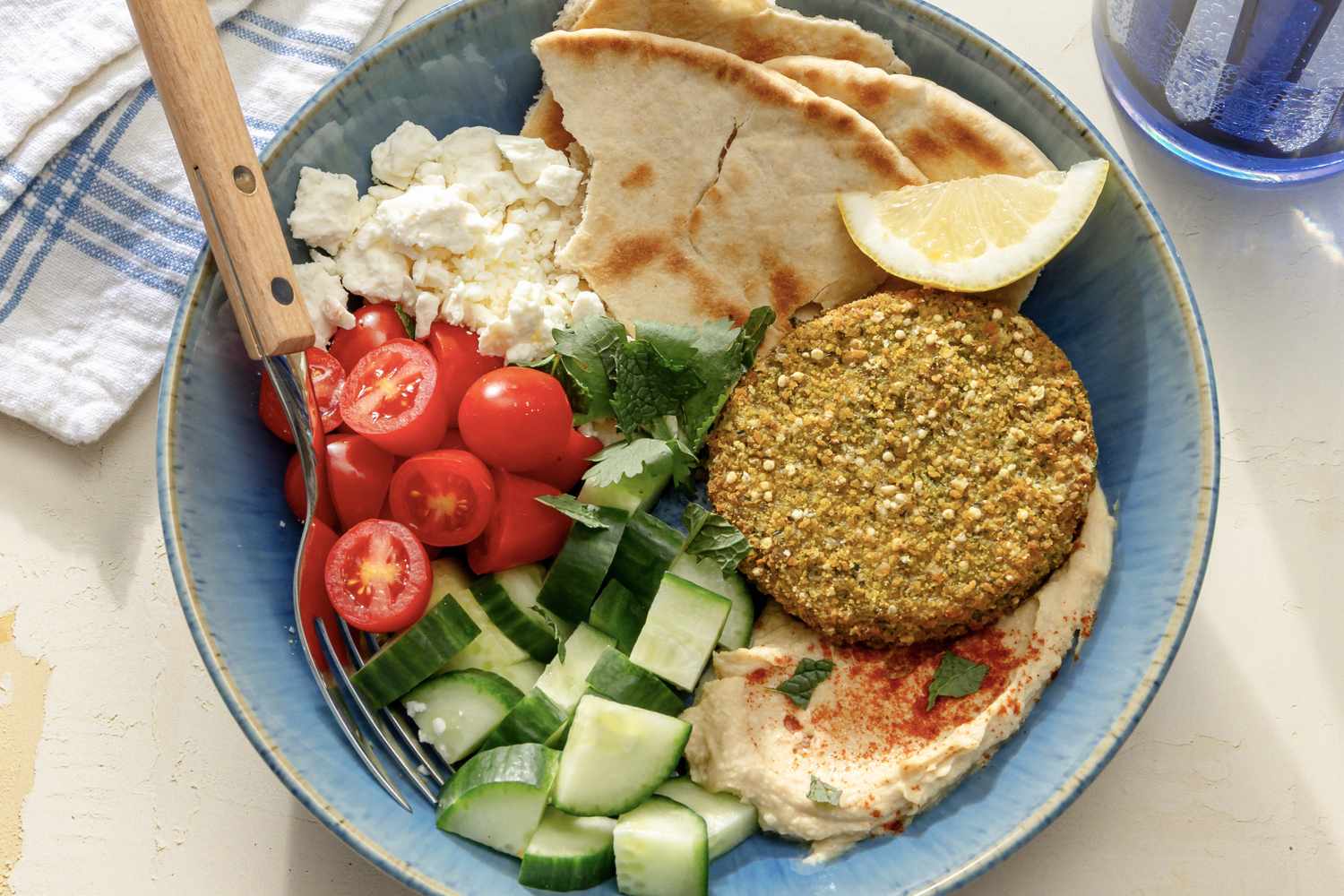 overhead view of Falafel Bowl - pita, feta, falafel, hummus, lemon slice, cucumbers, and grape tomatoes