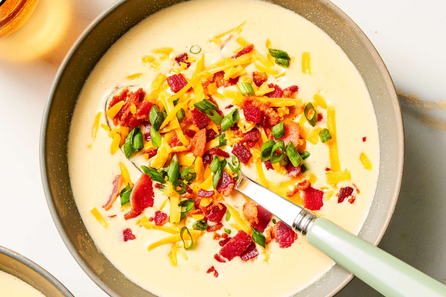 Bowl of loaded potato soup garnished with shredded cheese scallions and bacon with a spoon