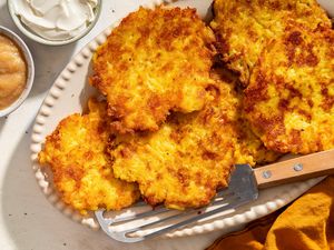 Plate of latkes with a spatula small bowls of sour cream and applesauce nearby