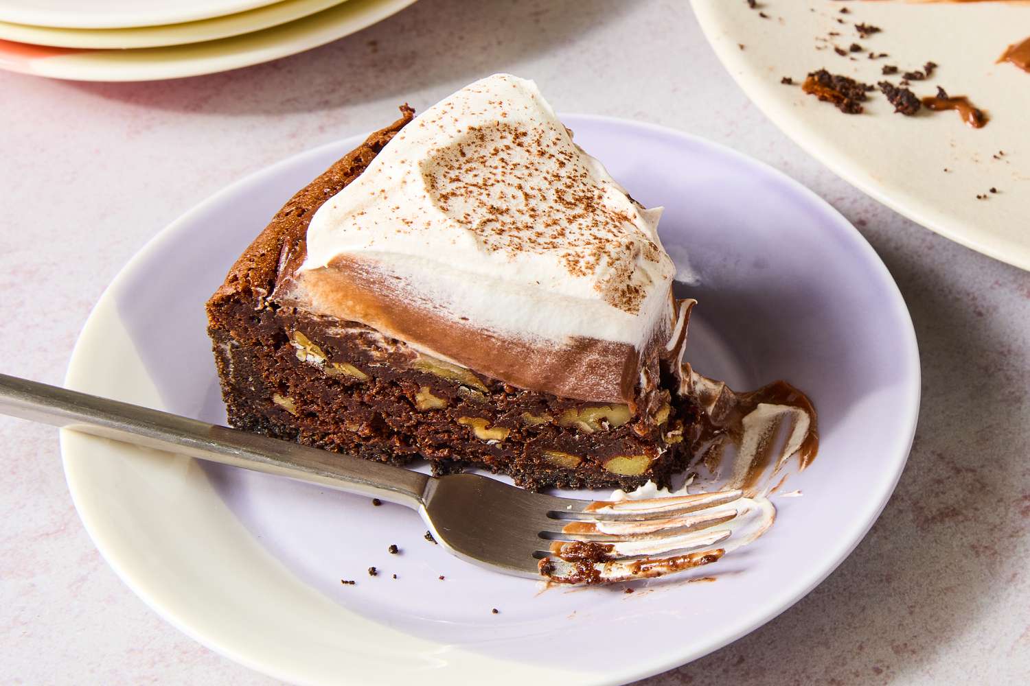 Closeup of a small multicolored plate with a slice of Mississippi Mud Pie with a fork next to a plate of the pie with several slices removed and a stack of empty plates