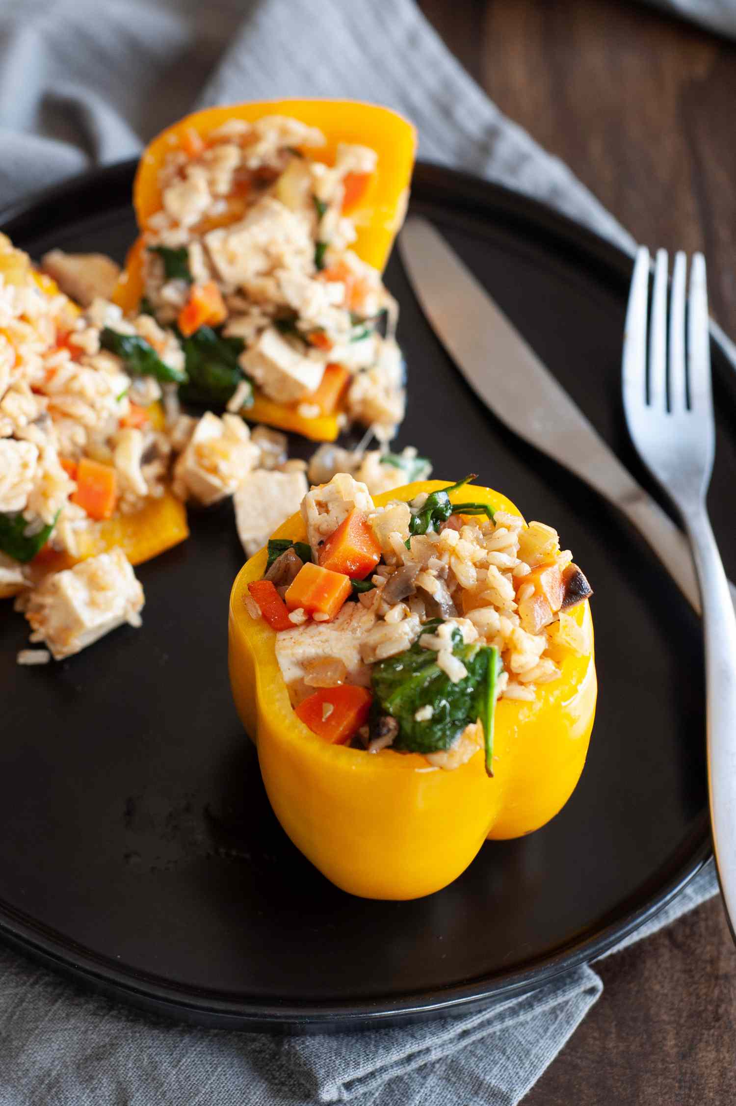 Cheesy rice, tofu, and mushroom stuffed peppers on a black plate