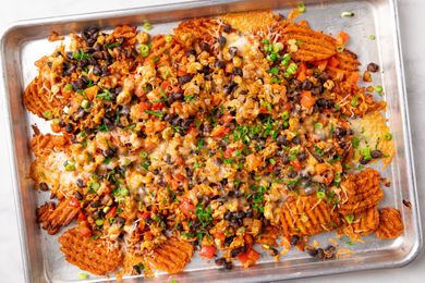 Wafflecut sweet potato slices topped with cheese beans tomatoes and green onions on a baking sheet