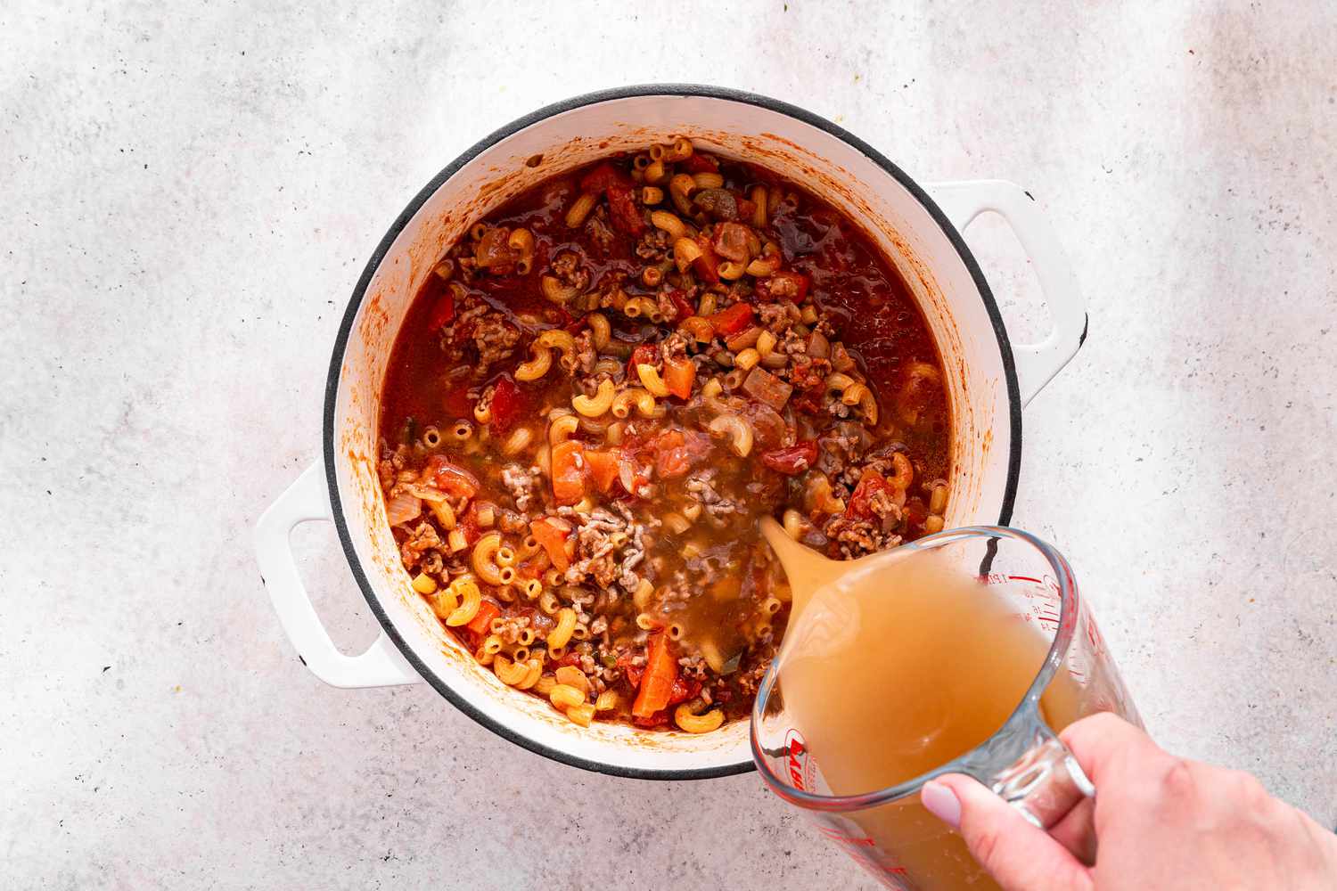 Beef Broth Added to Dutch Oven Using a Measuring Cup