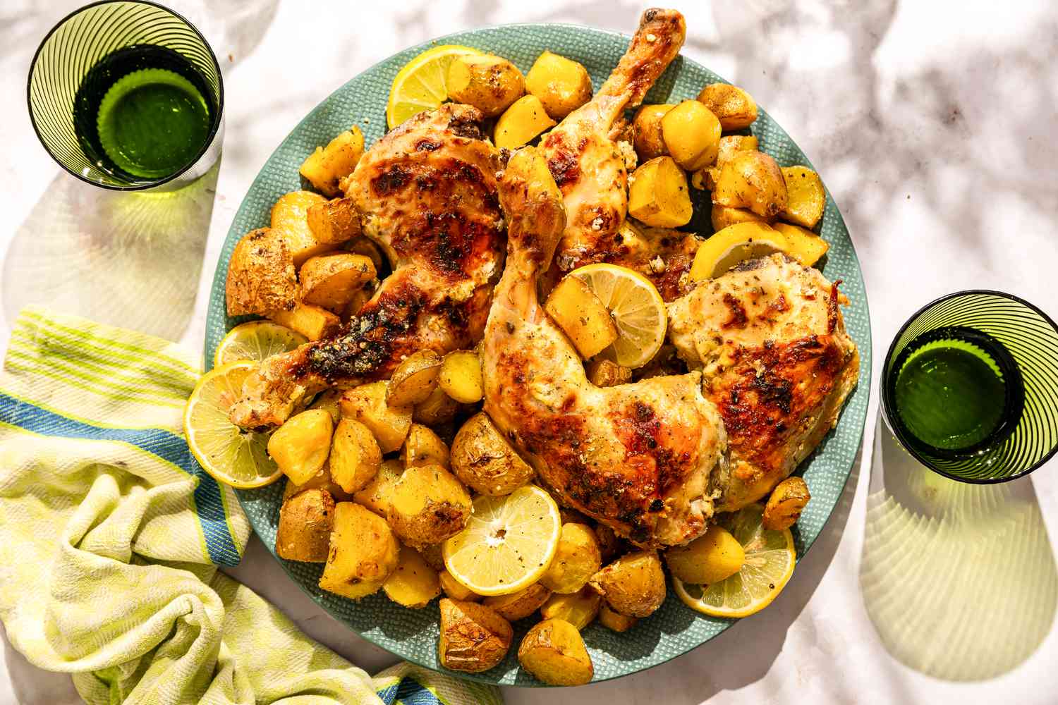 A large plate of Greek-style roast chicken with potaotes and lemon slices