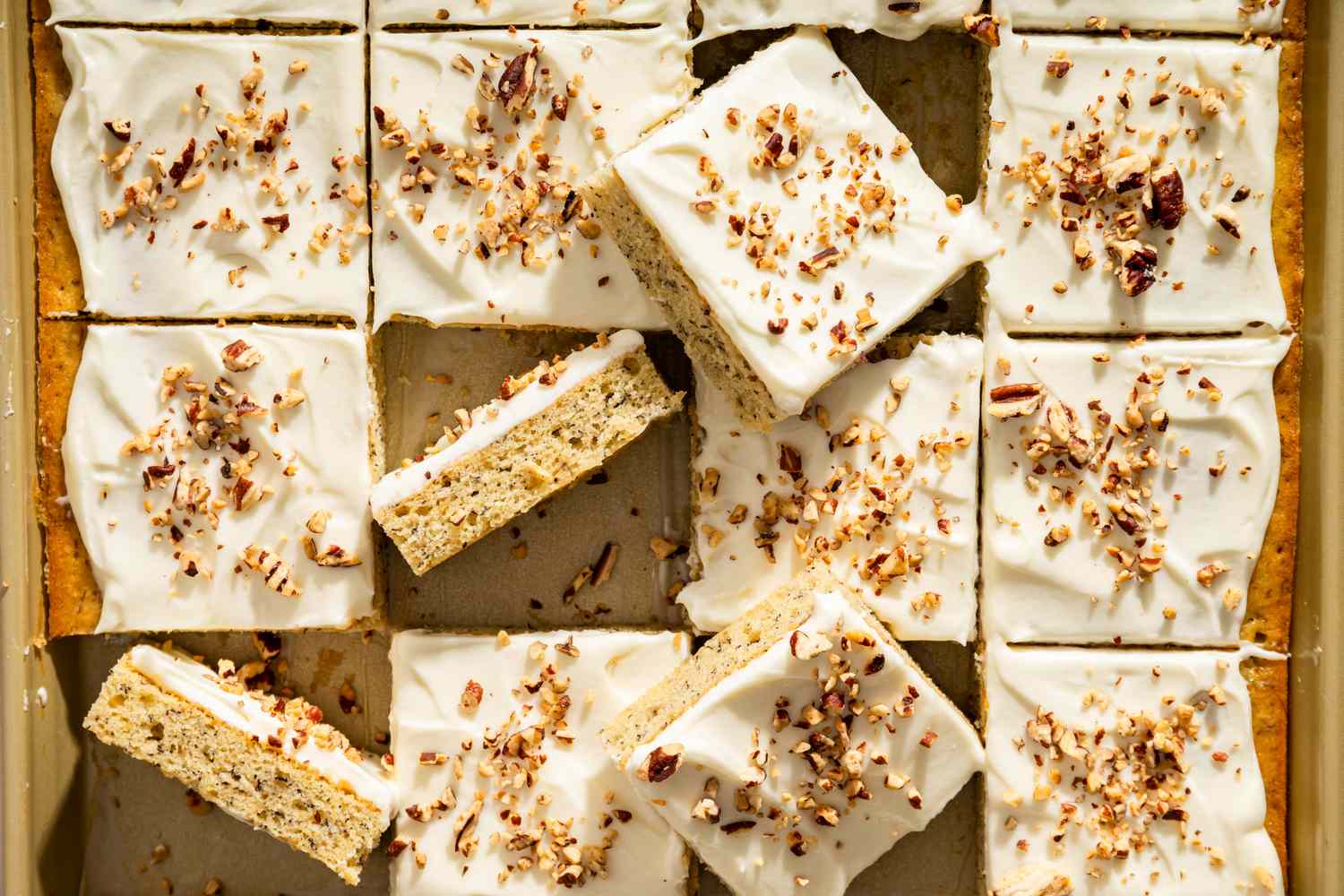 Banana bars with frosting and sprinkled nuts arranged in a grid