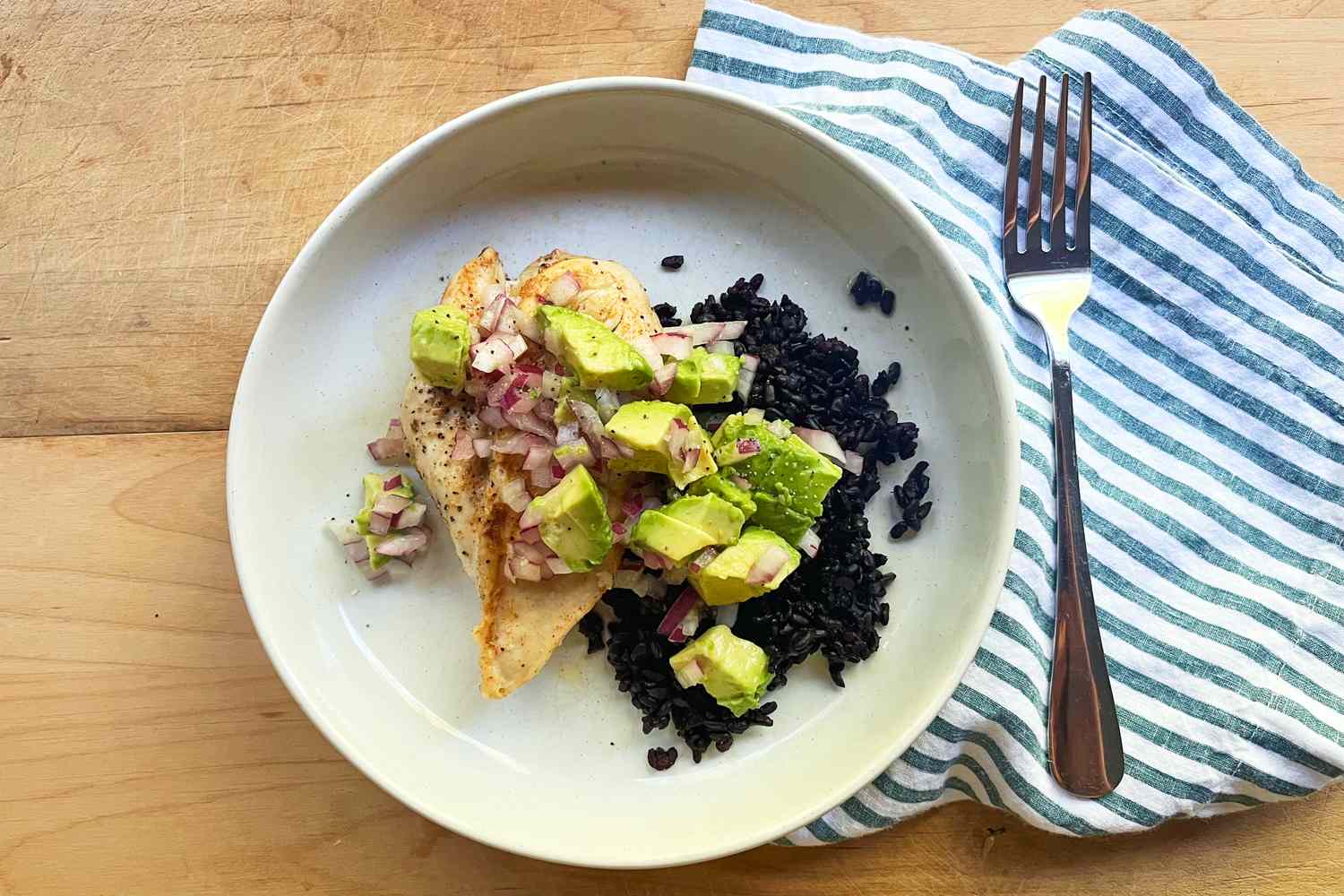 Plate of chicken topped with avocado salsa next to black rice fork placed to the side