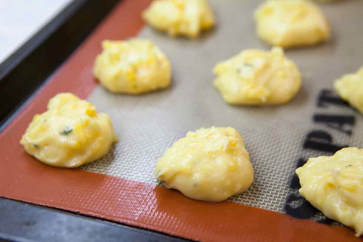 scoop cheese puff dough by spoonfuls onto a lined baking sheet