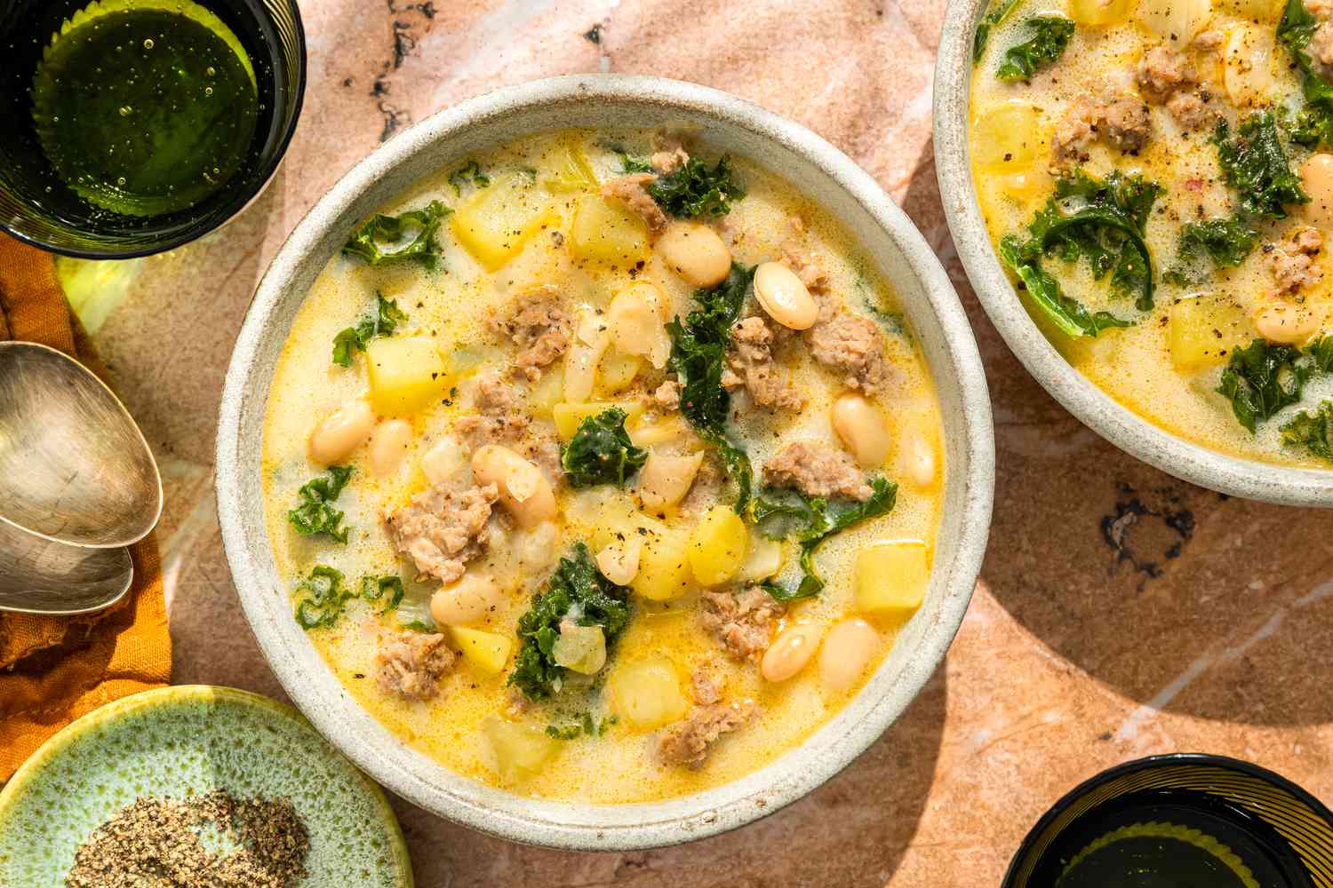 Overhead shot of two bowls with a cream based soup with beans, sausage, kale and potatoes