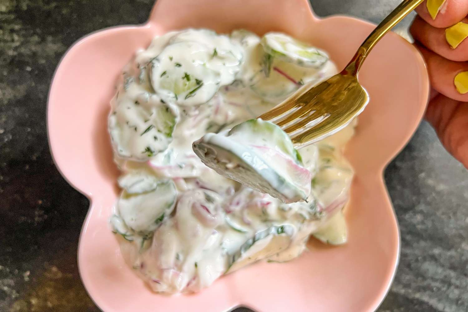 A bowl of cucumber salad with creamy dressing, a fork holds a piece