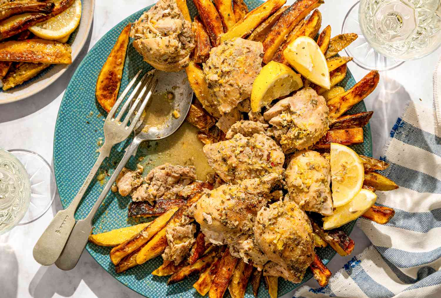 A dish of braised chicken served on a plate with fries and lemon wedges
