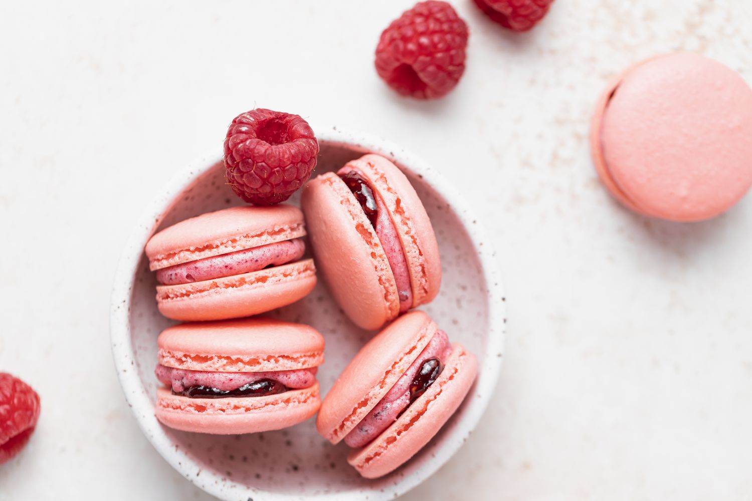 Raspberry macarons filled with raspberry buttercream in a small bowl.