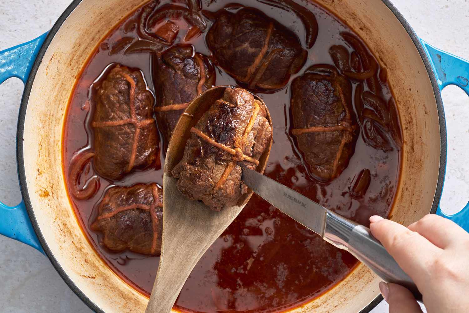 A rouladen lifted from Dutch oven and pierced with a knife to check if tender