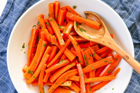 Overhead shot of a white shallow bowl with julienned carrots tossed in herbs and a wooden serving spoon