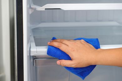 A person cleaning the inside of a refrigerator with a blue cloth