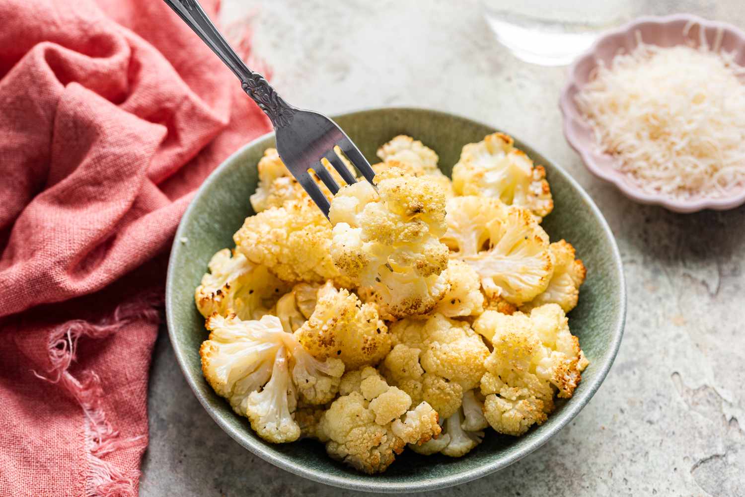 Roasted Cauliflower in a Bowl Next to Parmesan Cheese in a Small Plate 