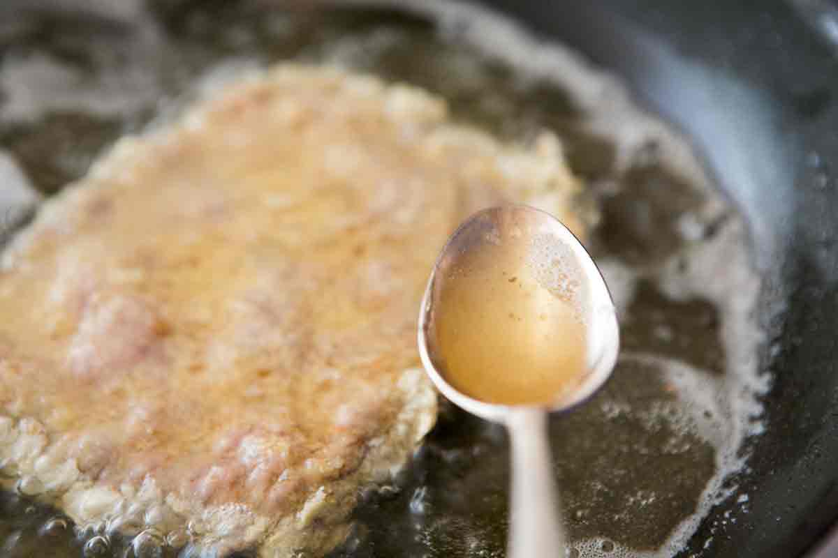 Pouring hot oil with a spoon over country fried sirloin in a pan