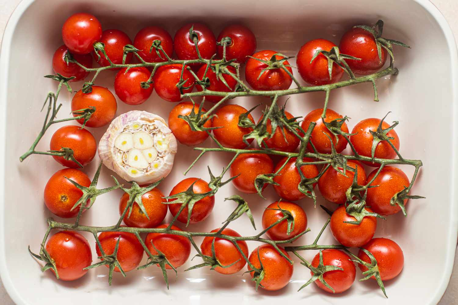Vined Cherry Tomatoes and Head of Garlic in a Baking Dish for Tomato Confit Recipe