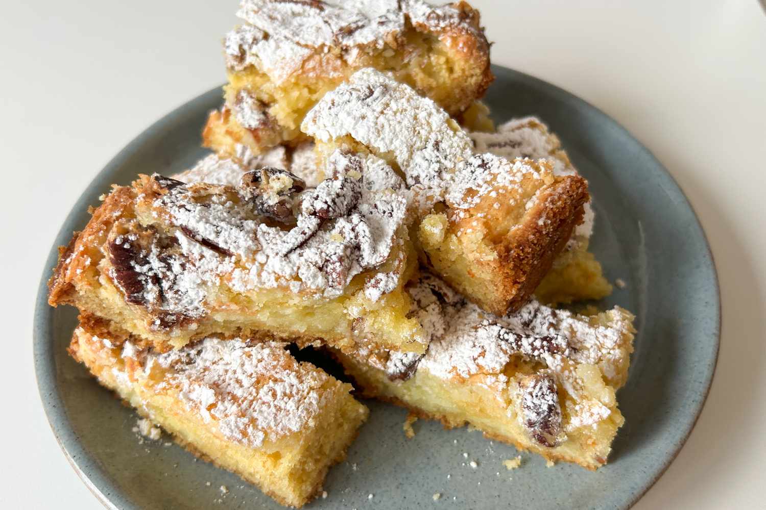 Ooey gooey dessert bars on a plate topped with powdered sugar served as a snack or treat