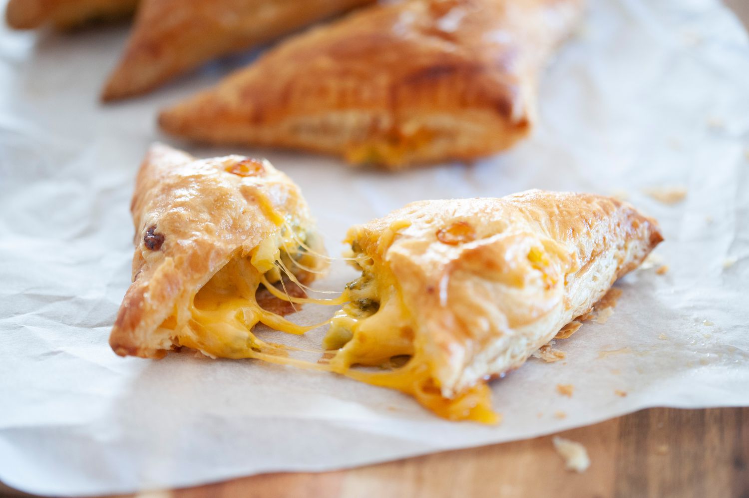 Broccoli and cheese hand pies on parchment paper with one split open to show the melted cheese and broccoli.