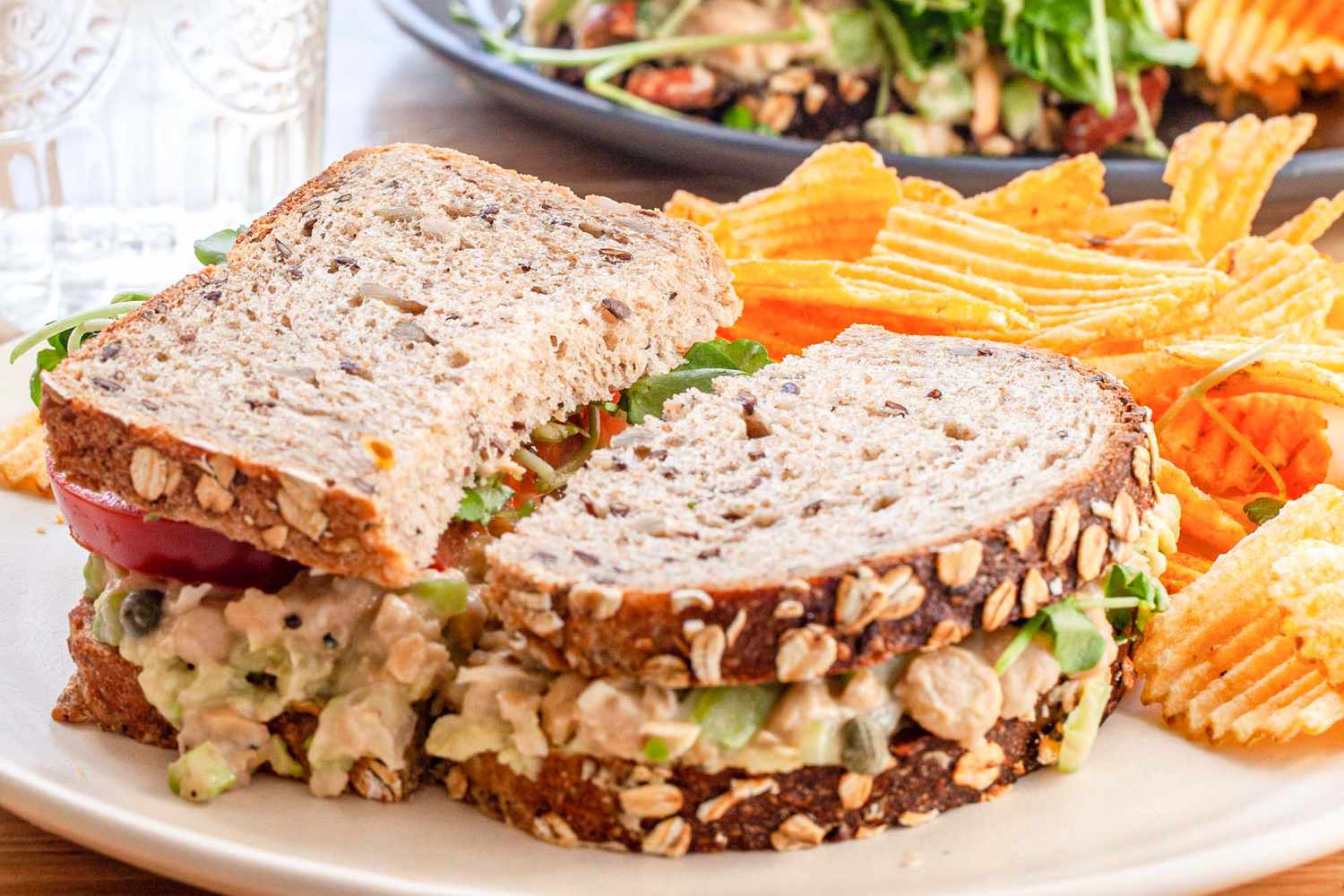 A chickpea salad sandwich on a plate with potato chips