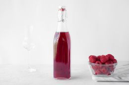 Fresh raspberry liqueur in a bottle next to a bowl of raspberries.