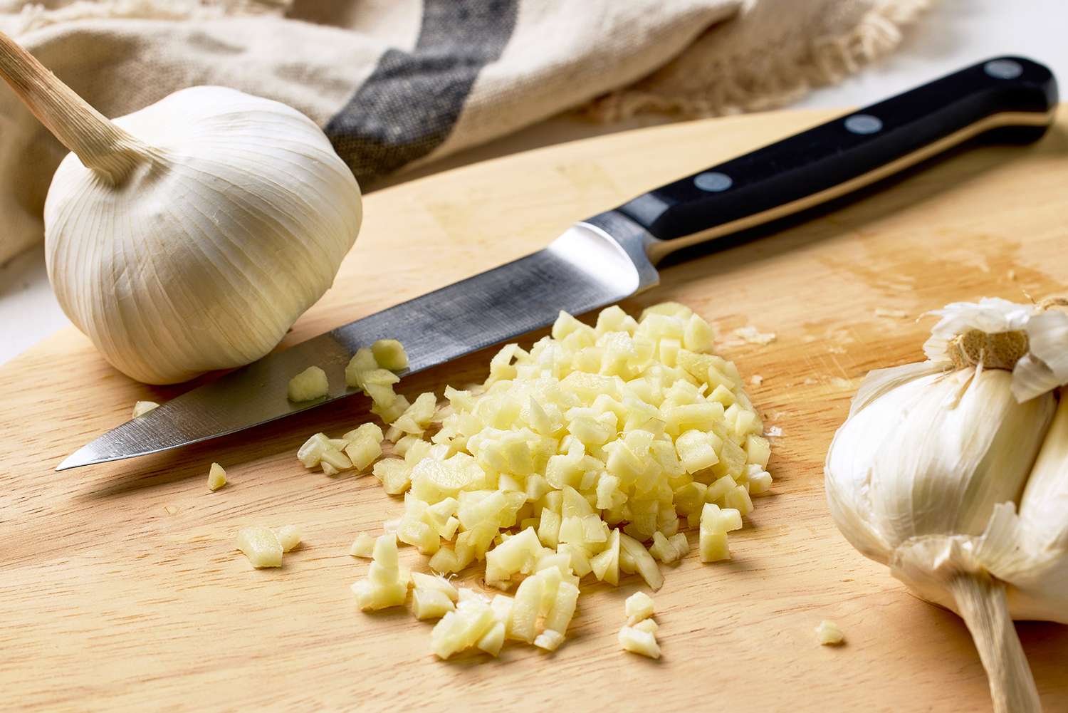 A cutting board with minced garlic a knife and whole garlic bulbs