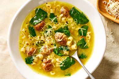 Overhead view of a white bowl of Italian wedding soup with spoon and topped with Parmesan cheese