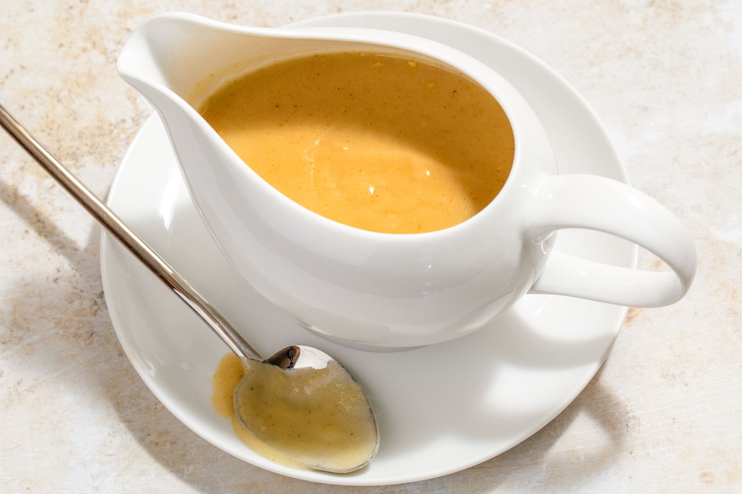 Angled view of a white gravy boat full of gravy on a white saucer with a spoon