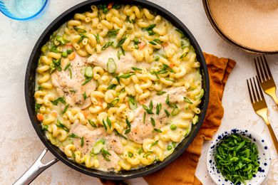 easy chicken primavera at a table setting with a bowl of sliced green onions, a bowl, and utensils on the counter