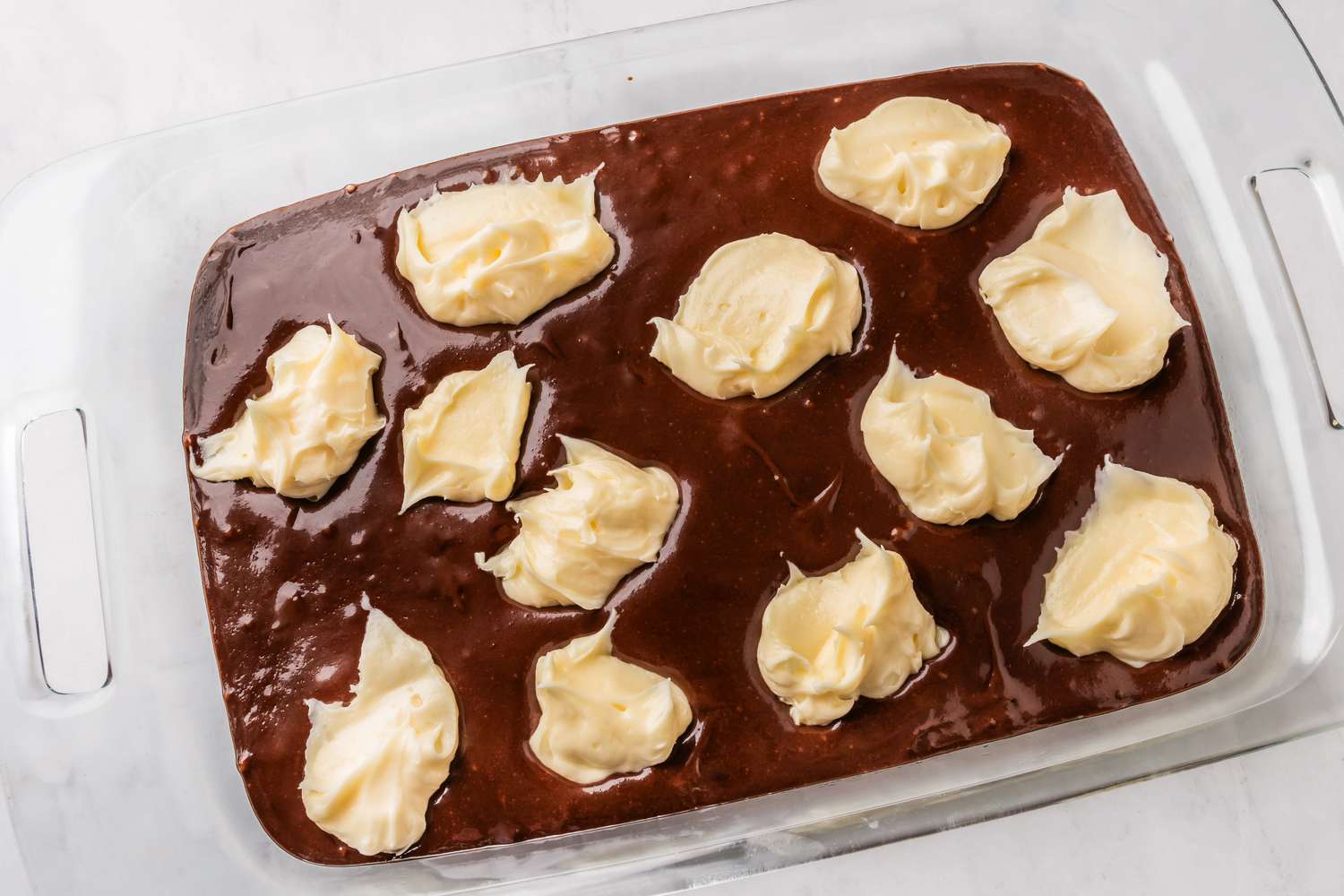 dollops of cream cheese filling added to chocolate batter in the pyrex dish for earthquake cake recipe