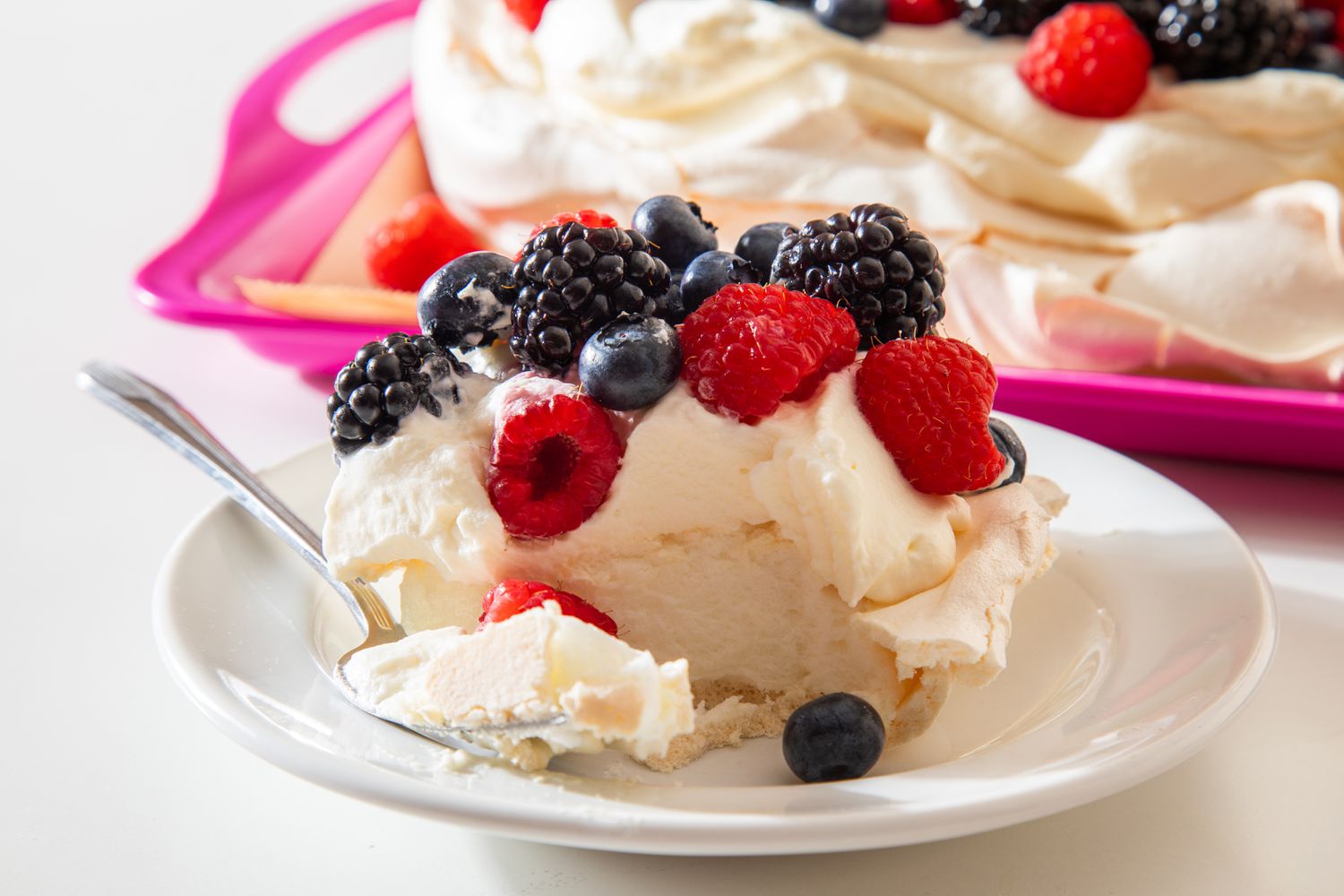 slice of berry pavlova on a plate next to the tray with the rest