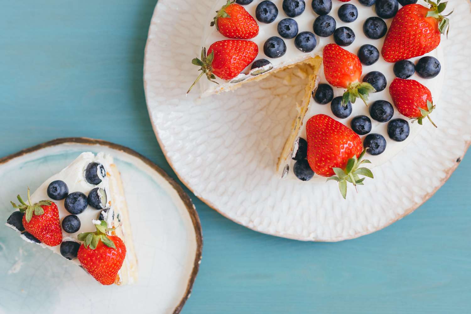 A cake with strawberries and blueberries, slice served separately