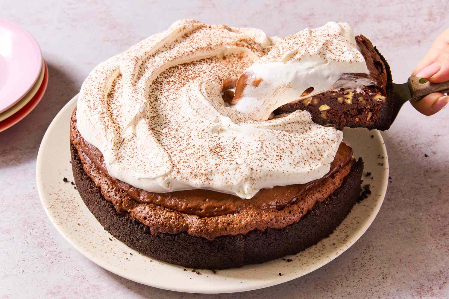 Image of a white plate of Mississippi Mud Pie with a hand holding a pie server and removing a slice on a pink background