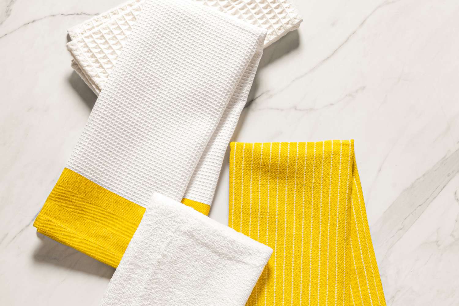 Yellow and white kitchen towels folded on a marble surface