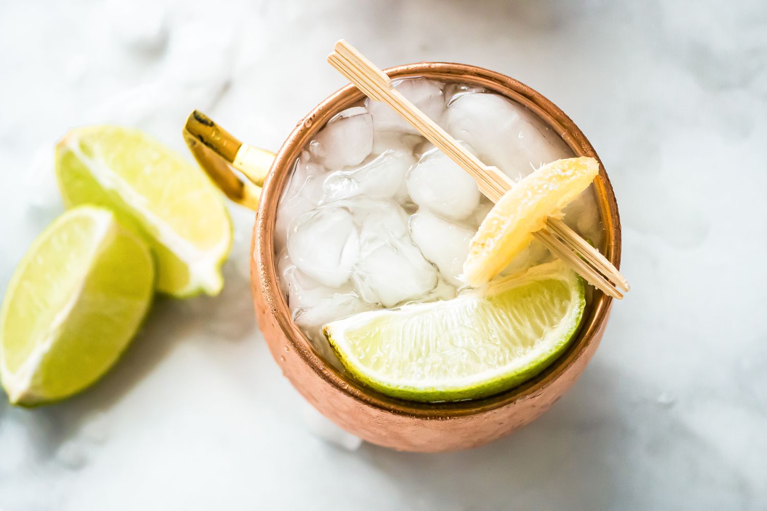 Mezcal Mule in Copper Mug with Candied Ginger and Lime Wedge, Next to Lime Wedges