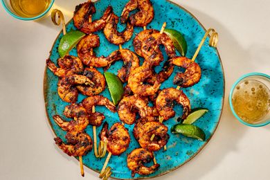Platter of shrimp skewers with lime wedges, served on a blue plate accompanied by drinks